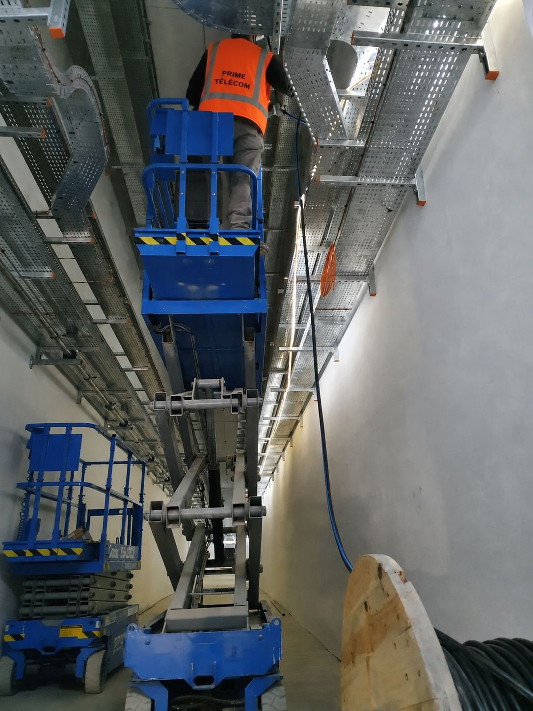 Technicien Prime Télécom installant un chemin de câbles en hauteur